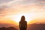 foto de pessoa olhando o nascer do sol nas montanhas, simbolizando despertar espiritual e conexão interior.