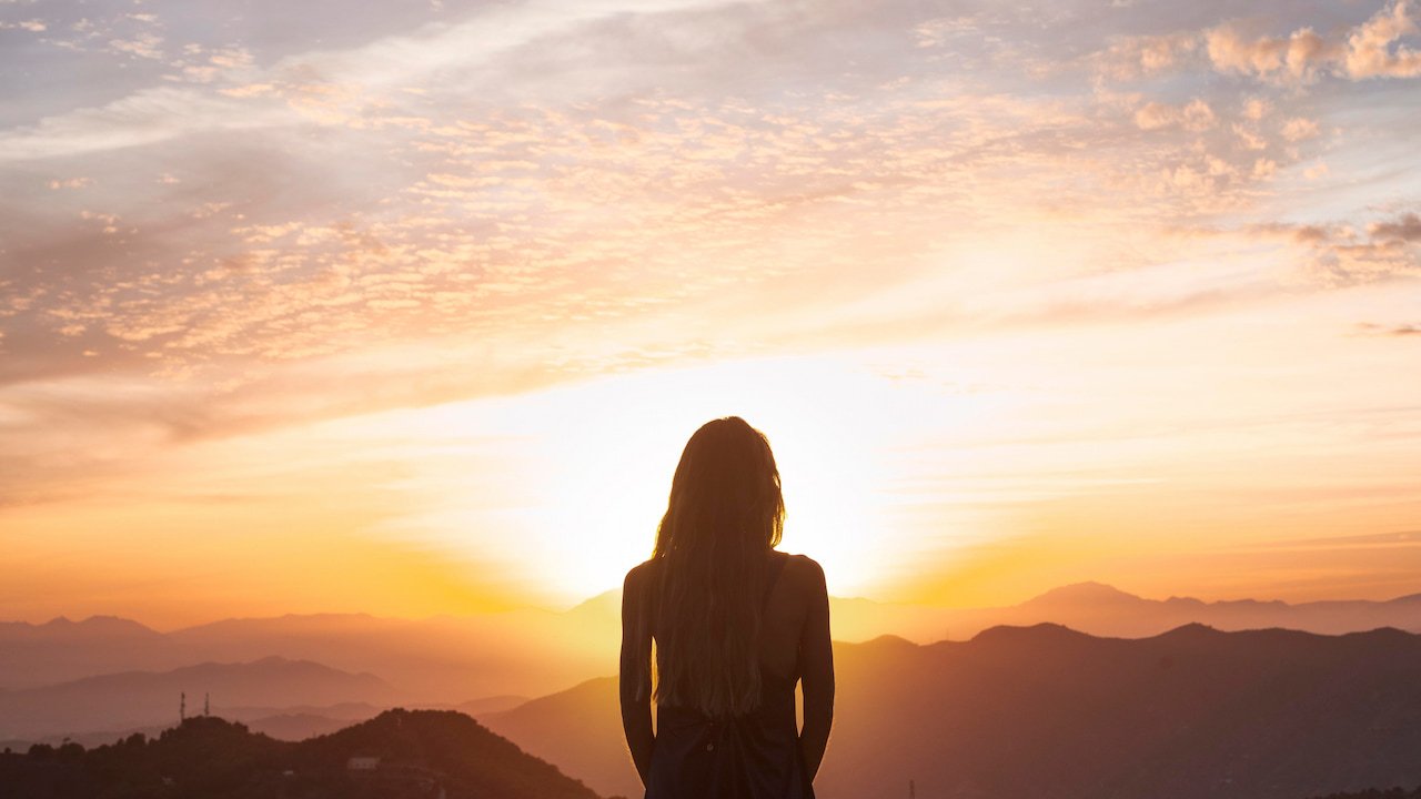 foto de pessoa olhando o nascer do sol nas montanhas, simbolizando despertar espiritual e conexão interior.